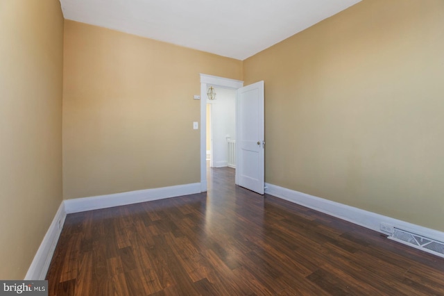 empty room with dark wood-type flooring, visible vents, and baseboards