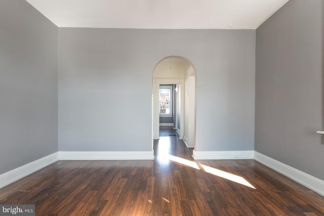 empty room with arched walkways, baseboards, and dark wood-style flooring