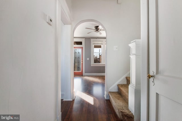 corridor featuring stairway, arched walkways, baseboards, and wood finished floors