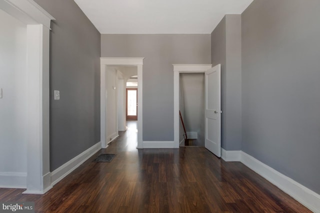 empty room featuring wood finished floors, baseboards, and arched walkways