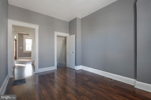 empty room with arched walkways, visible vents, baseboards, and dark wood-style flooring