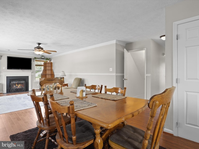 dining space featuring a lit fireplace, a textured ceiling, a ceiling fan, and wood finished floors