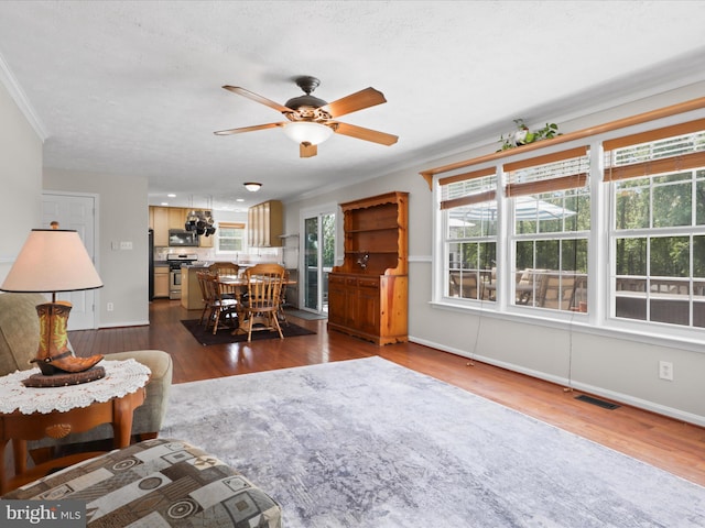 living room featuring baseboards, ceiling fan, dark wood-style floors, visible vents, and crown molding