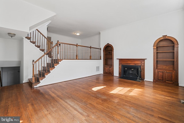 unfurnished living room featuring visible vents, a fireplace with flush hearth, wood finished floors, stairway, and crown molding