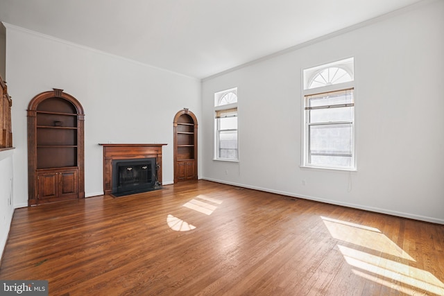 unfurnished living room with baseboards, a fireplace with flush hearth, wood finished floors, and crown molding