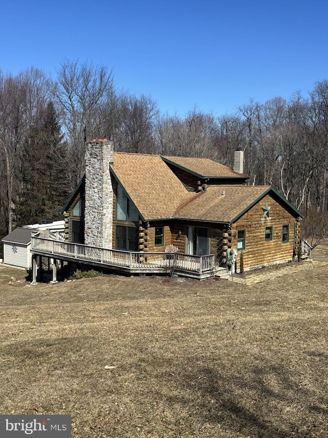 back of property featuring a wooden deck, roof with shingles, log exterior, and a chimney