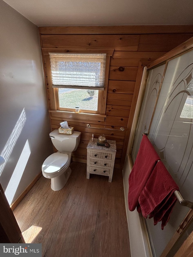 bathroom with wood finished floors, baseboards, a shower, wood walls, and toilet