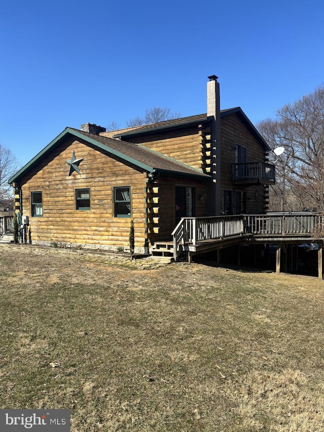 view of side of home featuring log siding, a balcony, a chimney, and a lawn