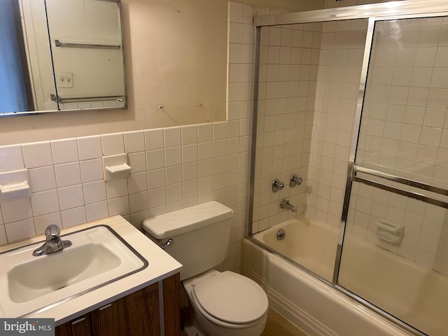 bathroom with enclosed tub / shower combo, vanity, toilet, and tile walls