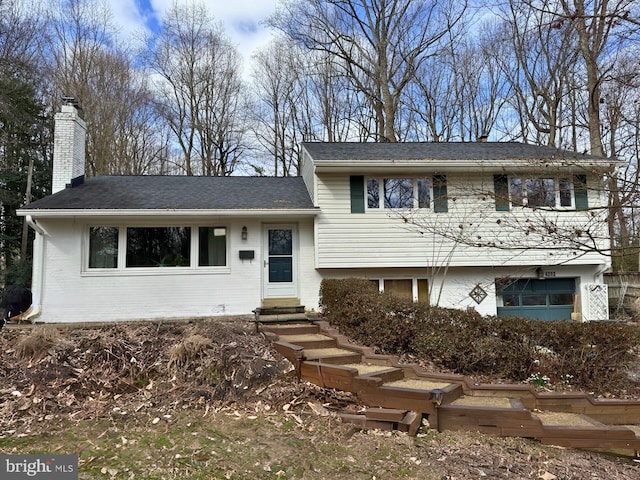 split level home with entry steps, brick siding, and a chimney