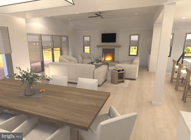 dining area featuring a lit fireplace, ceiling fan, and light wood finished floors