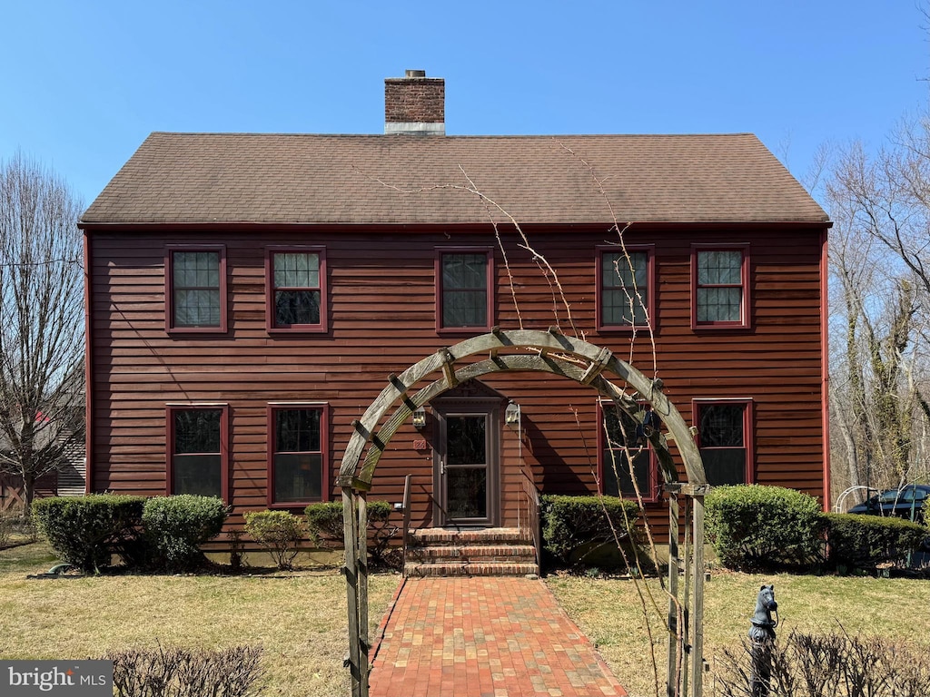 view of front of house featuring a front lawn, roof with shingles, and a chimney