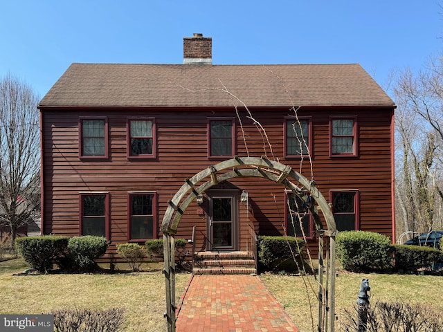 view of front of house featuring a front lawn, roof with shingles, and a chimney