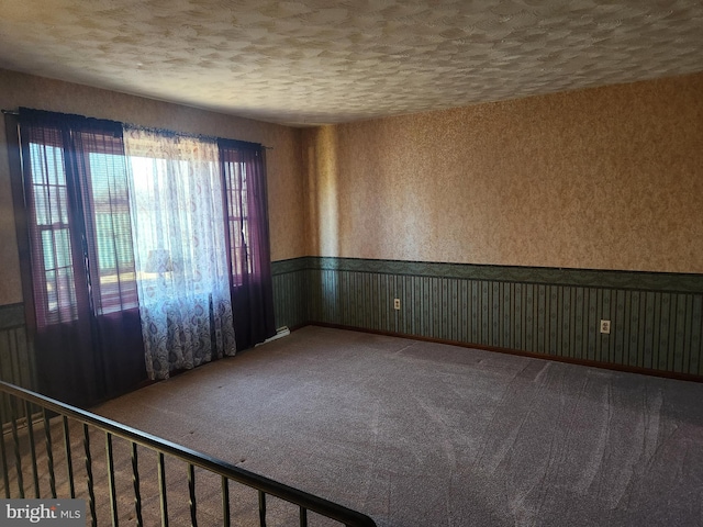 carpeted spare room with a wainscoted wall, a textured ceiling, and wallpapered walls