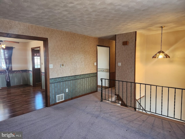 carpeted empty room featuring wood finished floors, a wainscoted wall, visible vents, wallpapered walls, and a textured ceiling