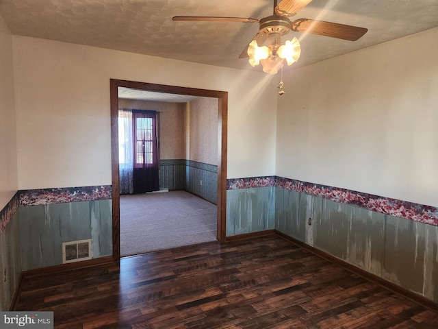 empty room with a ceiling fan, wood finished floors, visible vents, and a wainscoted wall