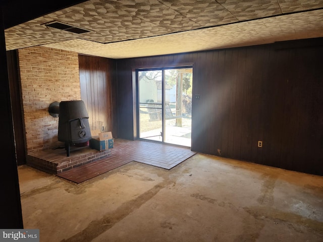 interior space with unfinished concrete flooring, visible vents, wood walls, and a wood stove