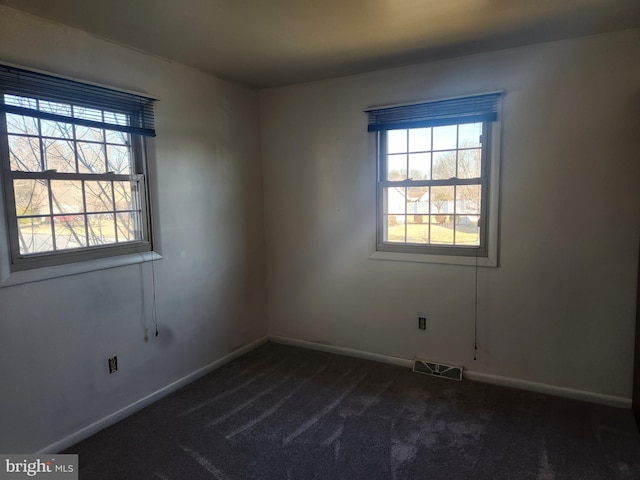 empty room featuring a wealth of natural light, visible vents, baseboards, and dark carpet