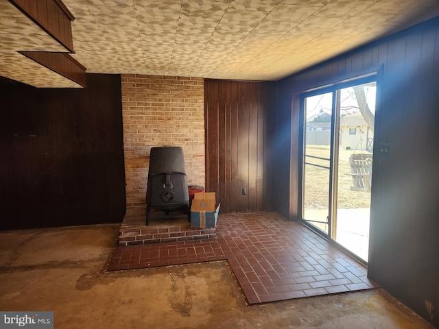 unfurnished living room featuring a wood stove and wood walls