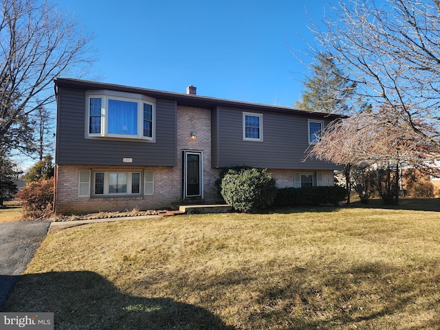 raised ranch featuring brick siding, a chimney, and a front lawn