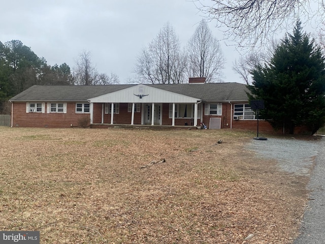 ranch-style home with driveway, a porch, a front yard, brick siding, and a chimney