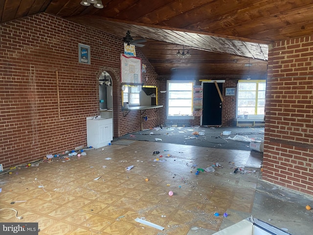 unfurnished living room featuring vaulted ceiling, wooden ceiling, and brick wall