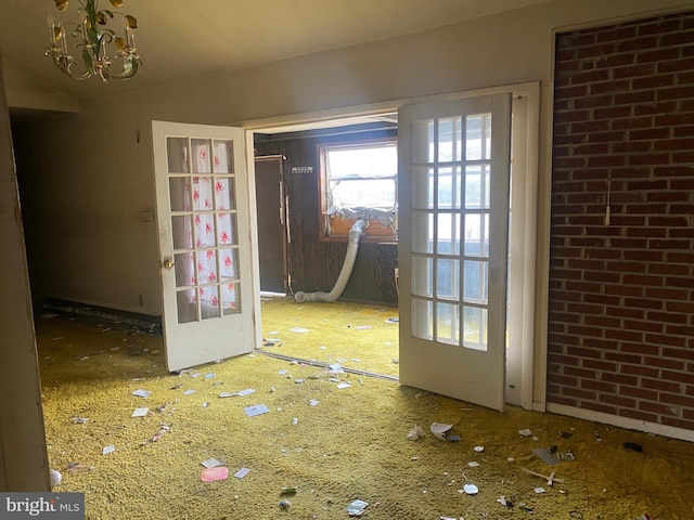 doorway to outside featuring lofted ceiling, a notable chandelier, and brick wall