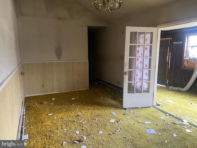 spare room with an inviting chandelier, lofted ceiling, and wainscoting