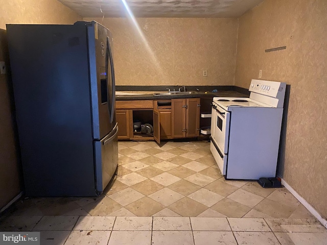 kitchen featuring dark countertops, stainless steel fridge with ice dispenser, a textured wall, electric range, and a sink