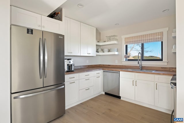 kitchen with a sink, appliances with stainless steel finishes, light wood-style floors, white cabinets, and open shelves