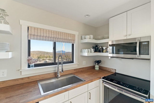 kitchen with a sink, open shelves, white cabinetry, stainless steel appliances, and wooden counters