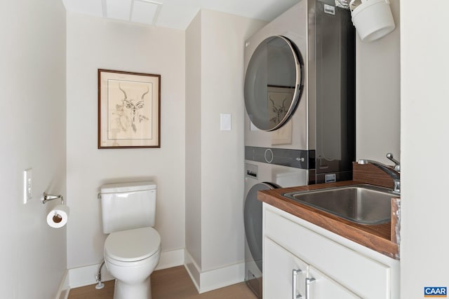 bathroom with vanity, wood finished floors, baseboards, stacked washing maching and dryer, and toilet