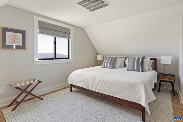 bedroom featuring visible vents, lofted ceiling, light wood-style floors, and baseboards