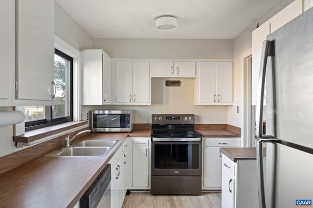 kitchen with butcher block counters, light wood-style flooring, appliances with stainless steel finishes, white cabinetry, and a sink