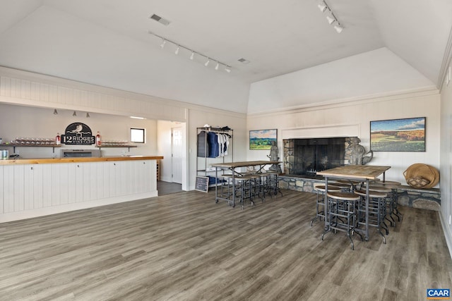 dining area with visible vents, track lighting, vaulted ceiling, a stone fireplace, and wood finished floors