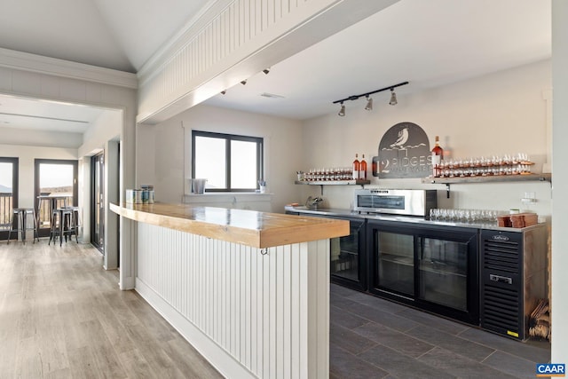 kitchen featuring stainless steel microwave, wood counters, wood finished floors, rail lighting, and lofted ceiling