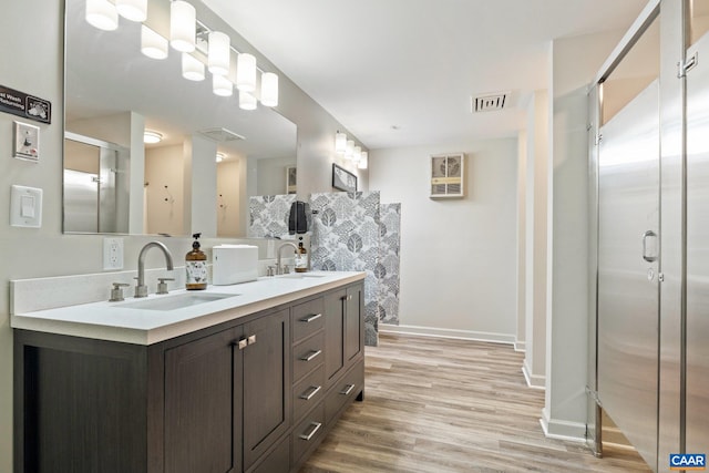 full bathroom featuring visible vents, double vanity, a stall shower, wood finished floors, and a sink