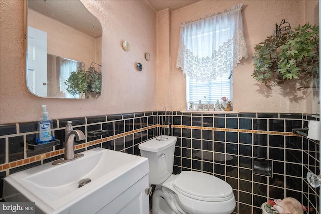 half bath with tile walls, toilet, a wainscoted wall, and vanity