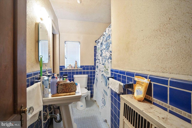 bathroom featuring tile walls, toilet, tile patterned flooring, wainscoting, and a shower with shower curtain