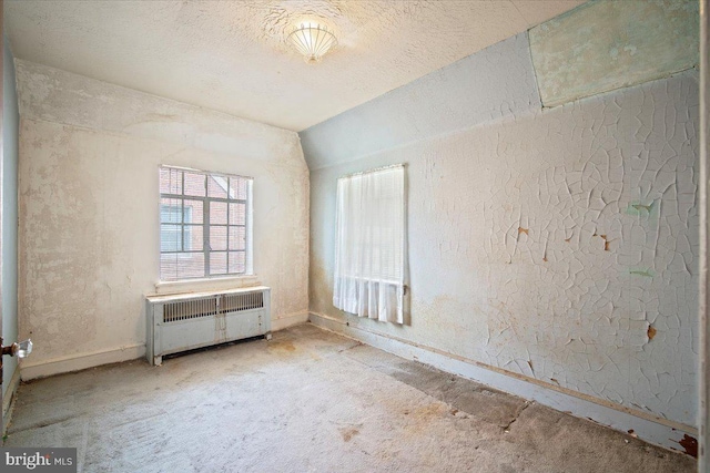 unfurnished room with light colored carpet, a textured wall, baseboards, and radiator heating unit