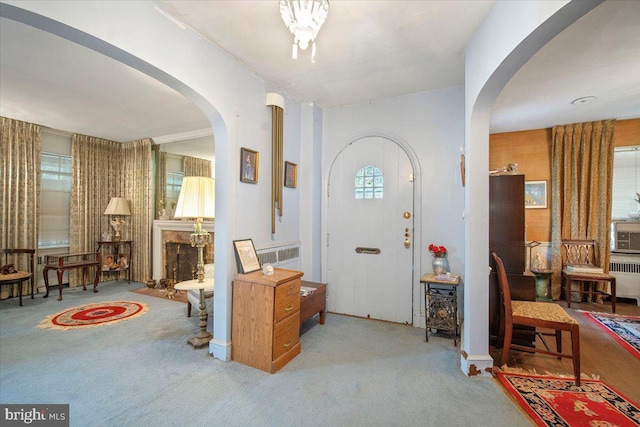 carpeted foyer with arched walkways, radiator, and a fireplace with raised hearth