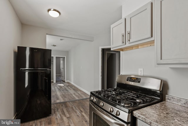 kitchen featuring baseboards, freestanding refrigerator, wood finished floors, white cabinets, and gas stove