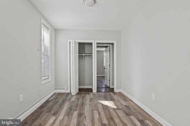 unfurnished bedroom with wood finished floors, baseboards, and a closet