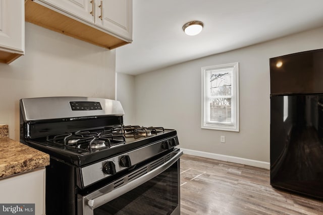 kitchen featuring light wood finished floors, baseboards, freestanding refrigerator, white cabinets, and gas stove