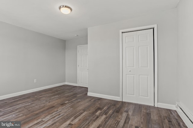 unfurnished bedroom with a closet, baseboards, baseboard heating, and dark wood-style floors