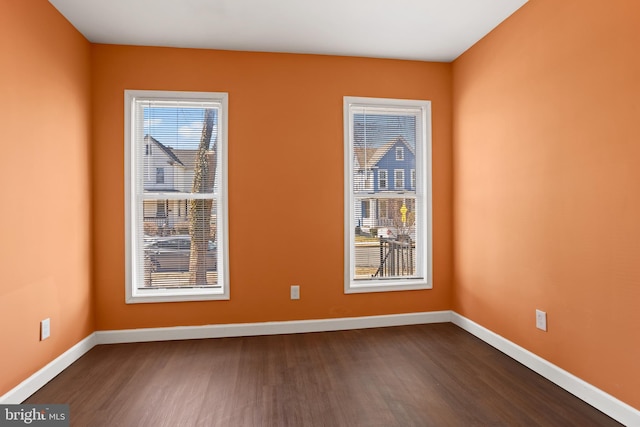 spare room with baseboards, dark wood-type flooring, and a healthy amount of sunlight