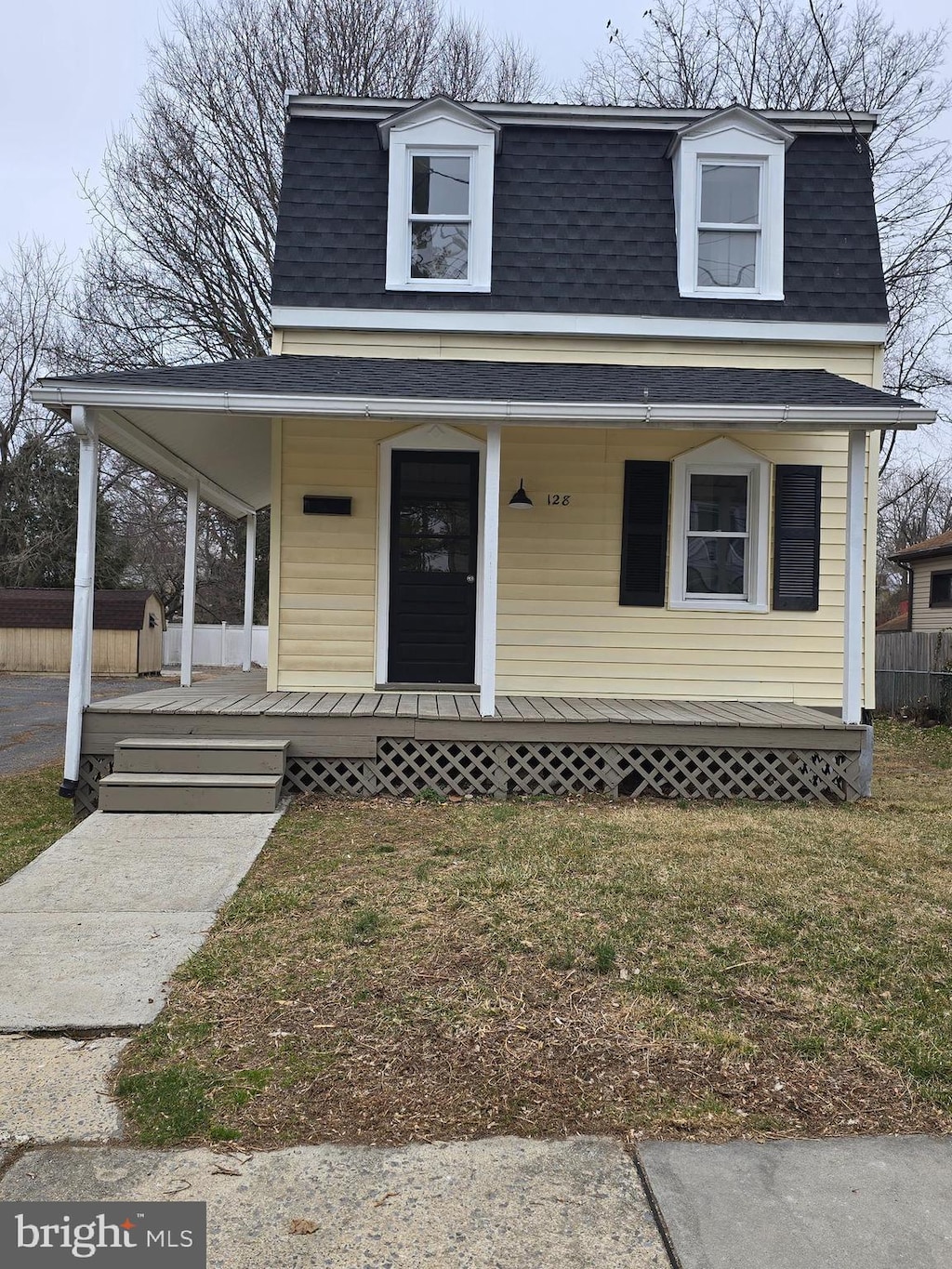 second empire-style home with a porch, mansard roof, and roof with shingles