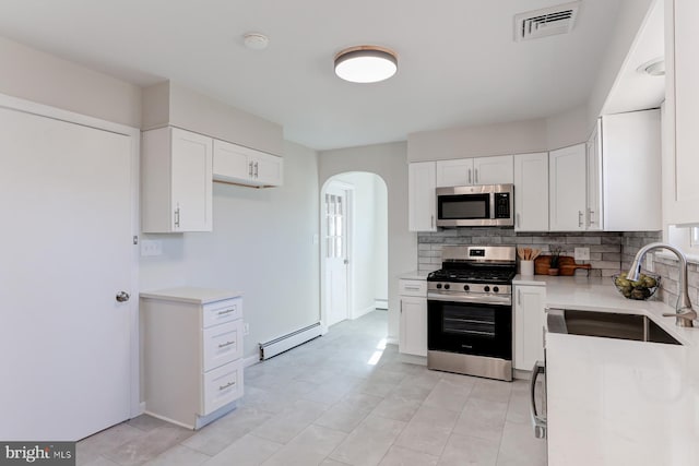 kitchen featuring visible vents, a baseboard heating unit, stainless steel appliances, arched walkways, and light countertops