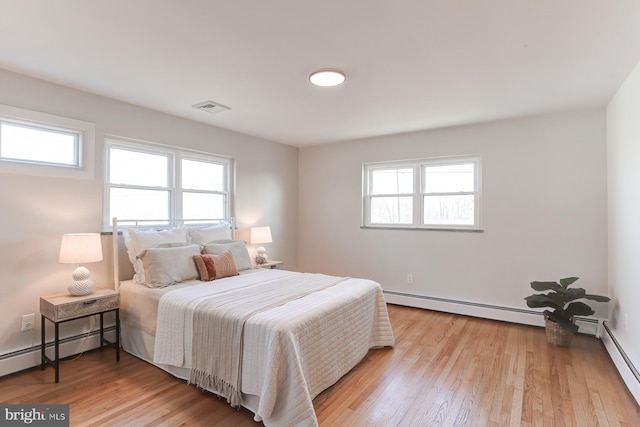 bedroom featuring a baseboard heating unit, multiple windows, visible vents, and light wood finished floors