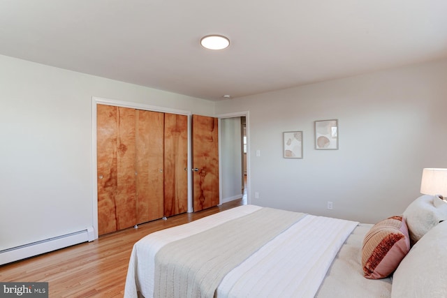 bedroom featuring a baseboard heating unit, a closet, and light wood finished floors